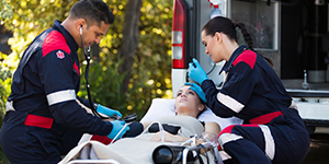 Paramedics treating a patient on a stretcher at the rear of an ambulance.